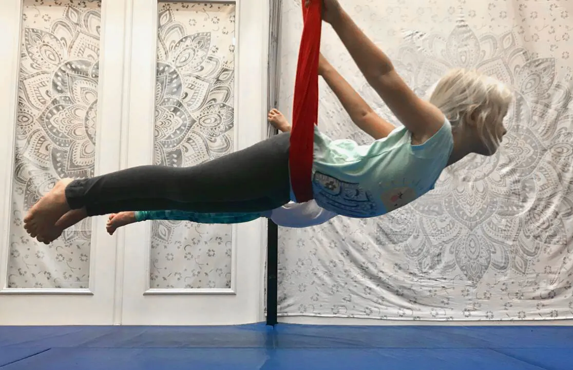 A student flies face-down in a red aerial silk